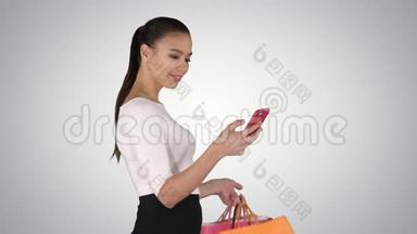 年轻的女人带着购物袋走路，在梯度背景上用手机说话。