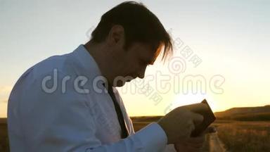商人在夕阳的温暖光线下在公园里玩平板电脑游戏。 男人在智能手机上玩游戏。 开心快乐