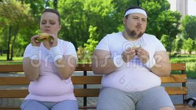 肥胖的年轻夫妇吃汉堡包，<strong>沉迷于</strong>垃圾食品，缺乏意志力