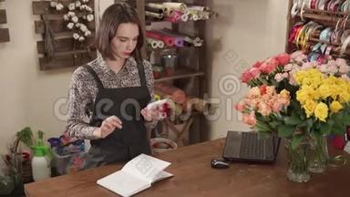 花卉工作室的女售货员正指望着一台智能手机计算器和写作