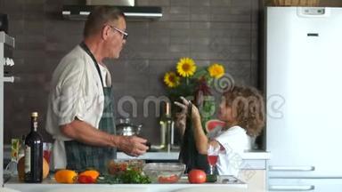孙子在厨房帮爷爷做饭.. 一个成熟的男人在男孩身上穿厨房围裙。 父亲`