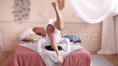 快乐的年轻女子在家里跳在床上做一个翻滚。 装饰室。 前段录像