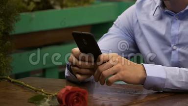 男人用<strong>手机</strong>坐在桌边，红玫瑰躺在前面，等待<strong>约会</strong>