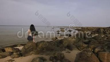 美丽的女孩坐在靠近海岸的岩石上，眺望远方..
