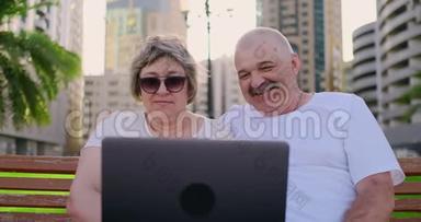 今年夏天，一对快乐的老夫妇坐在一个现代城市的长凳上，手提电脑在棕榈树上