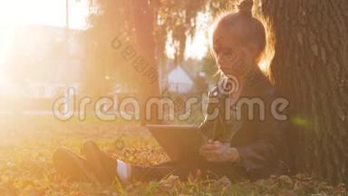 日落时分，带着石碑的小女孩坐在秋天公园的一棵树下。