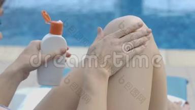女士在她的腿上涂<strong>润肤露</strong>，按摩动作在游泳池旁休息