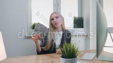 有钱的轻松女人。 优雅的年轻金发女郎，穿着商务套装，坐在办公桌旁，端着电脑和植物