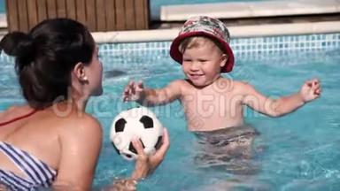 一个快乐的孩子和他的母亲在游<strong>泳池里玩耍</strong>，试图去踢足球