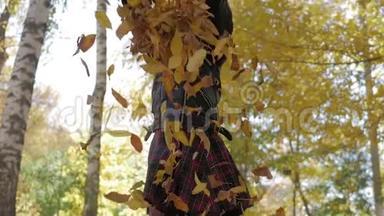 可爱的快乐学校女孩把落叶扔了起来，在秋天的森林里玩。 美丽的女孩在玩