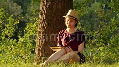 教育和商业。 女孩<strong>坐在</strong>公园里的一棵绿<strong>树下</strong>，在一块石碑上工作。