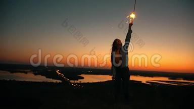 年轻女子手里拿着火花，看着山上令人惊叹的日落