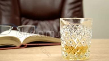 酒精饮料在水晶蜕膜。 在玻璃里，把威士忌倒在背景的木桌<strong>上</strong>，<strong>一张</strong>椅子<strong>上</strong>坐下。 开放书籍