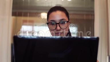 戴眼镜的女商人用电脑和手机工作，坐在办公室的桌子上，心情很好。 特写镜头。 高清。