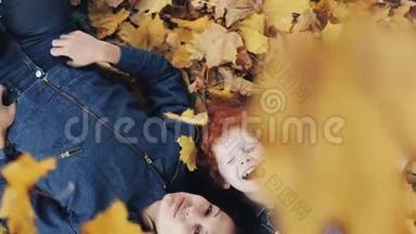 一位美丽的母亲和她可爱的女儿躺在秋天公园的一片黄叶上。 他们看着<strong>镜头</strong>，<strong>俯视</strong>