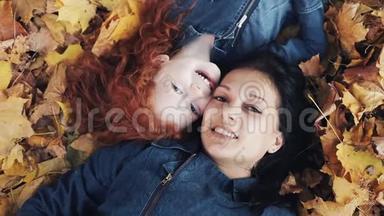 一位美丽的母亲和她可爱的女儿躺在秋天公园的一片黄叶上。 他们看着<strong>镜头</strong>，<strong>俯视</strong>