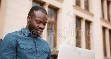 非裔美国人商务人员坐在长凳上，在笔记本电脑上工作。 在公园里用笔记本电脑工作的商人