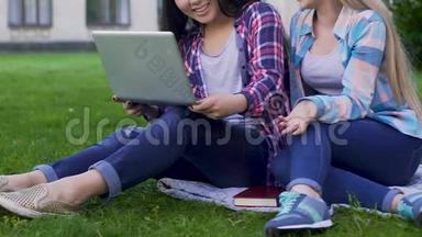 两名女生在草坪上拿着笔记本电脑，进行讨论、交友