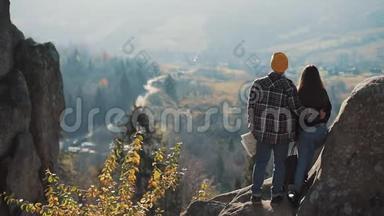 年轻的旅游夫妇相爱，站在岩石上，欣赏美丽的景色。 拜访著名游客的男人和女人