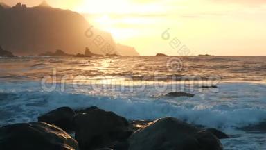 慢动作。 在加那利群岛特内里费的贝尼霍海滩上，美丽的夕阳下的海浪。 巨大的海浪冲击着