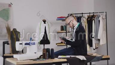 一位英俊的<strong>时装</strong>设计师坐在工作室的桌子上，画草图来裁剪新的<strong>时装</strong>系列。