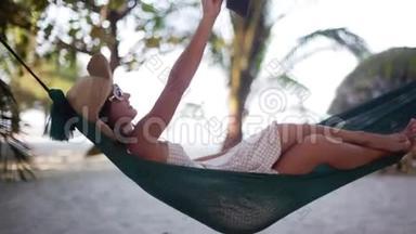 放松的女孩戴着太阳镜和帽子自拍手机<strong>销售</strong>手机躺在吊床之间的棕榈树。 1920x1080