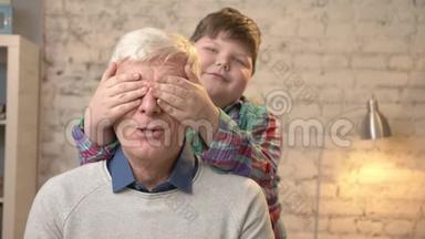 年轻的胖孩子用手闭上祖父`眼睛。 猜猜是谁。 游戏，恶作剧.. 幸福的家庭观念。 家庭