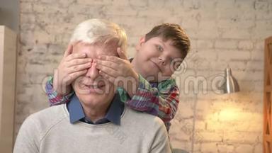 年轻的胖孩子用手闭上祖父`眼睛。 猜猜是谁。 一场游戏，恶作剧.. 孙子看着摄像机