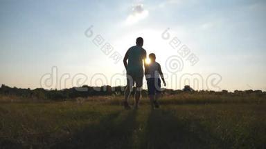 日落时分，父亲和儿子在田野上散步，互相<strong>牵着</strong>手的剪影。 快乐的家庭花时间