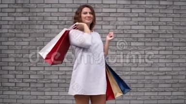 一个购物后带着包裹的女孩，心情很好，靠在石头墙上。 慢动作。