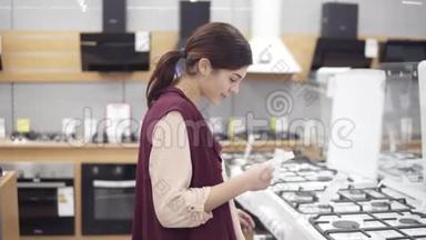 20`的年轻女孩在五金店寻找完美的炊具。 她检查价格，打开烤箱