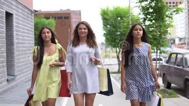 三个漂亮的女朋友购物后带着包裹沿着街走。 慢动作。 高清高清