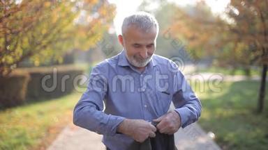 英俊的老人穿上灰色夹克。 白发苍苍的胡须老头走在秋天的公园里.. 黄色背景