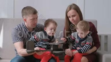 一家人的爸爸妈妈和两个双胞胎兄弟坐在沙发上玩木飞机。