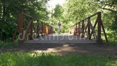 一个人骑自行车穿过公园里的桥。 慢动作