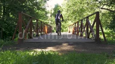 一个人骑自行车穿过公园里的桥。 慢动作