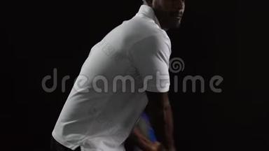 穿白色马球的肌肉网球运动员在黑色背景下击球，慢