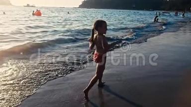 一个赤脚的<strong>小女孩</strong>在晚阳的温暖光线下沿着大海在潮湿的沙子上<strong>奔跑</strong>的缓慢运动。 粗心和粗心