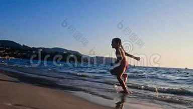 一个赤脚的小女孩在晚阳的温暖光线下沿着大海在潮湿的沙子上奔跑的缓慢运动。 粗心和粗心
