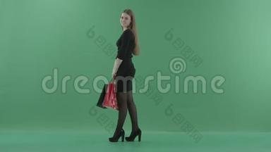 漂亮的笑女人穿着黑色小裙子，摆着购物袋。 她站在演播室里反对
