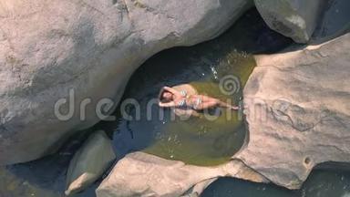 妇女享受在透明的河水鸟瞰洗澡。 美丽的女人穿着比基尼躺在河中无人机的视野中。