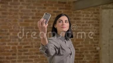 <strong>棕色短发</strong>的年轻美女用手机自拍并摆姿势拍照，砖墙背景