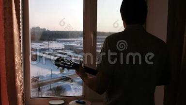 演奏乐器。 男人`剪影在窗台附近弹吉他。