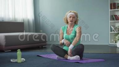 <strong>身穿运动服</strong>、坐在瑜伽垫上按摩肩膀的金发老年妇女