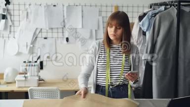 服装设计企业家正在检查纸张、缝纫草稿和看智能手机。 她正在检查每一个切口