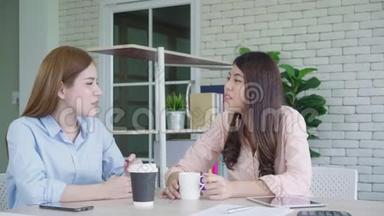 两名年轻的亚洲<strong>女大学生</strong>或同事在办公室喝咖啡和交谈，不同的群体。