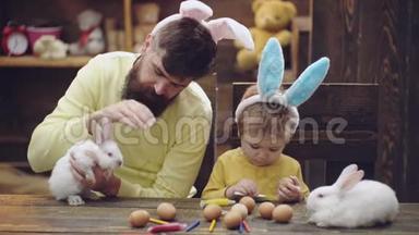 幸福的家庭正在为复活节<strong>做</strong>准备。 可爱的小男孩戴着<strong>兔子</strong>耳朵。 一个男人和一个男孩把复活节彩蛋涂在