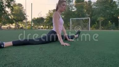 年轻自信的女人坐在公园的足球场上，晨练，健身模特锻炼