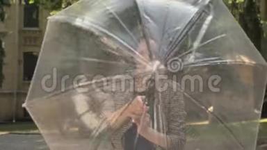 年轻迷人的女孩白天在公园里打开雨伞，夏天在公园里旋转雨伞，看着镜头