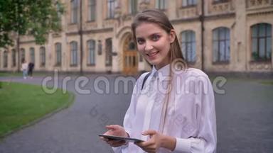 年轻漂亮的女学生在夏天的平板电脑上工作，微笑着，看着摄像机，交流理念
